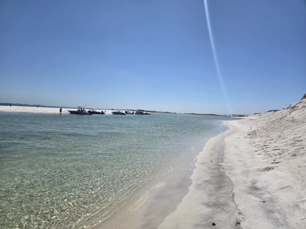 The white shores and shallow waters of Sand Island, a popular spot to anchor a Pensacola Pontoons boat rental, with boats relaxing in the background.