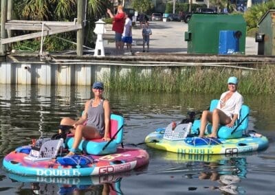 Two women driving motorized inflatable float boats with battery-powered motors near the docks in Pensacola Beach.